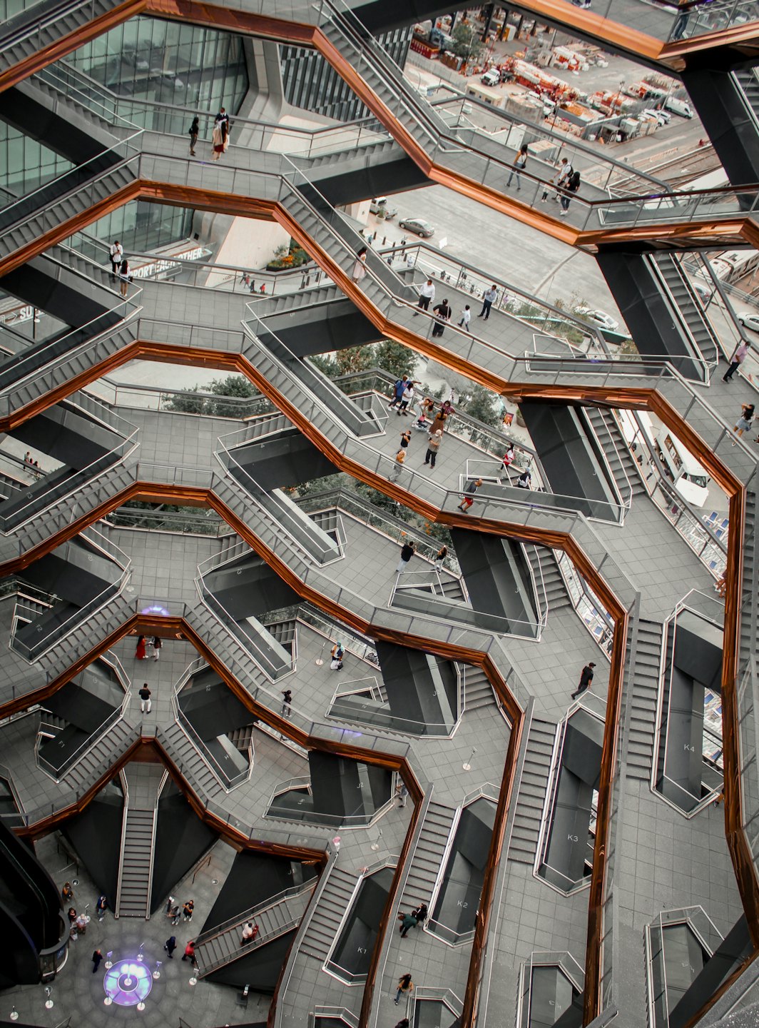 People navigate a modern building with grey staircases and copper railings.