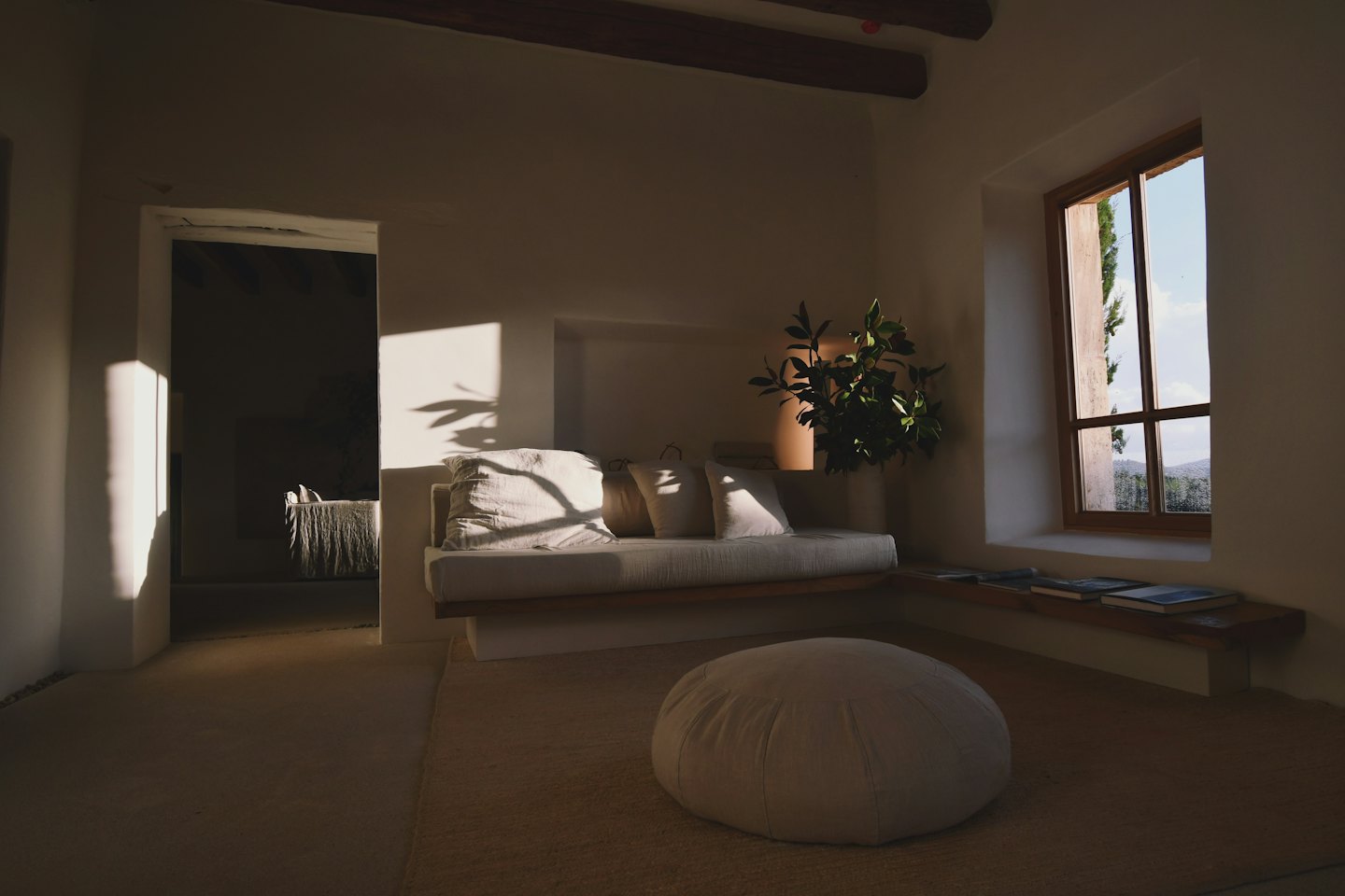 Sunlight streams into a minimalist living room with a sofa and ottoman.