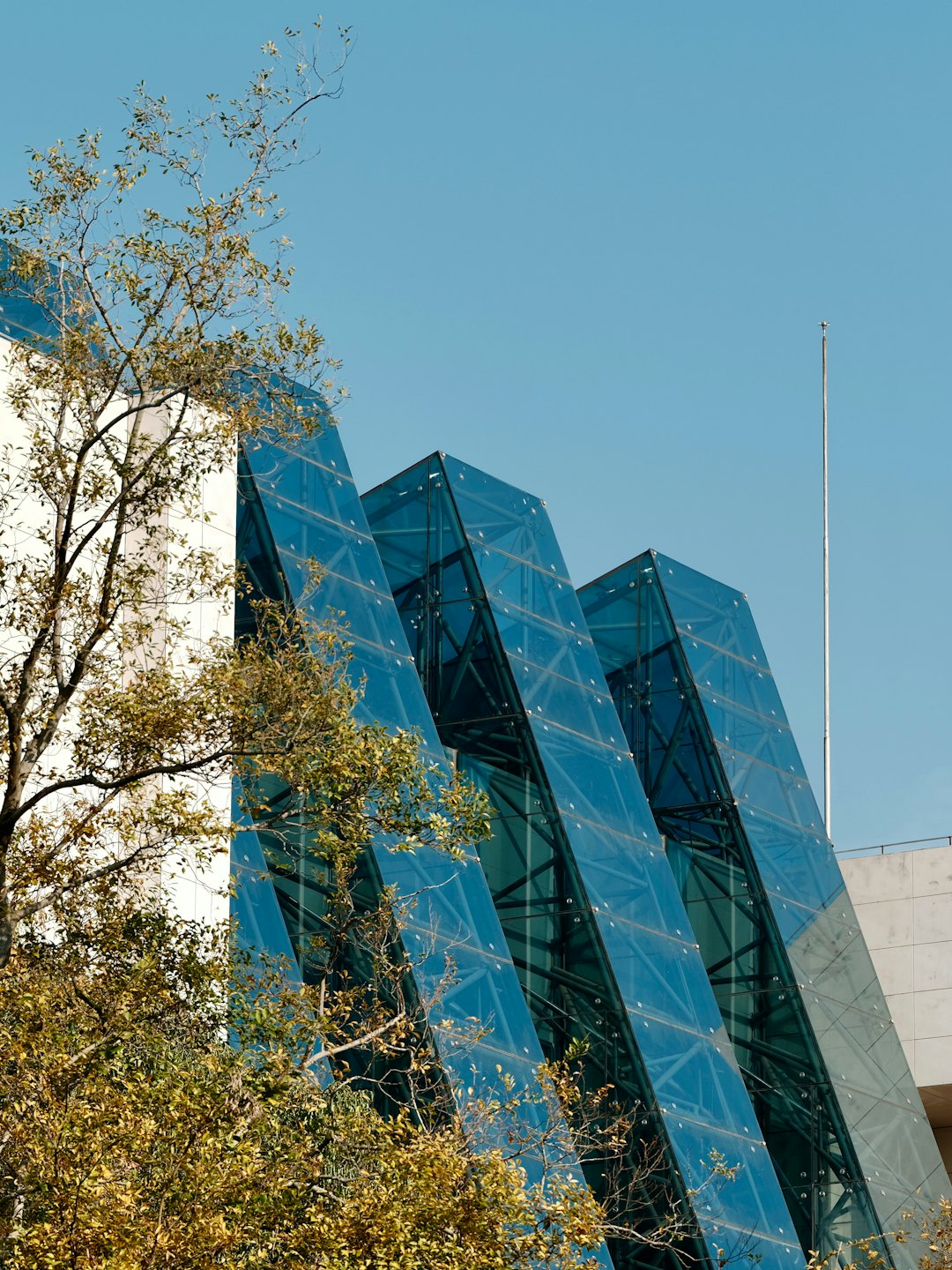 Modern blue glass building with geometric shapes near green trees.